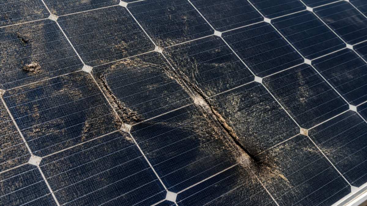 Close-up of solar panel surface showing visible cracks, discoloration from debris accumulation, and burnt edges on individual cells with environmental dirt buildup